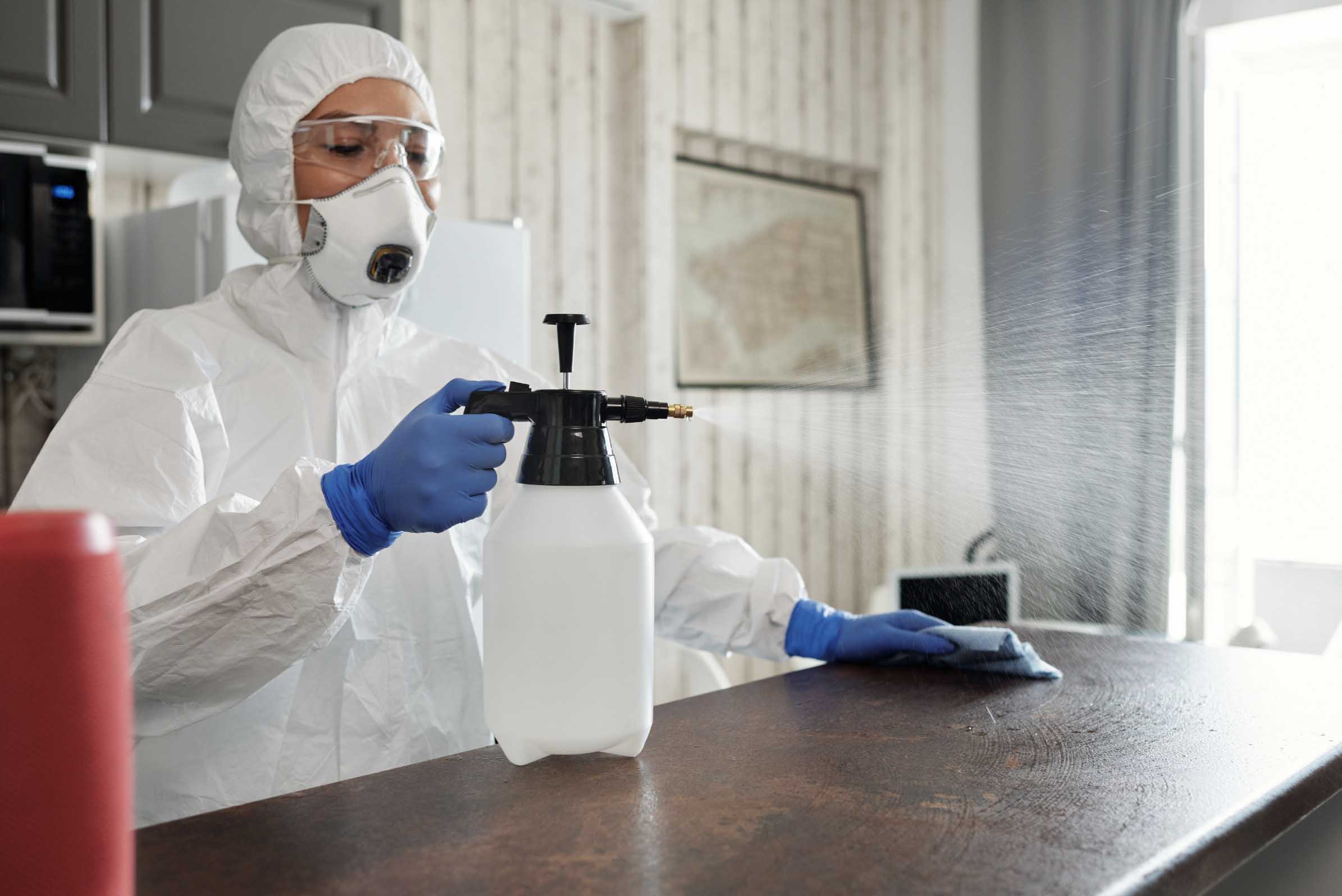 A woman in protective gear disinfecting a business